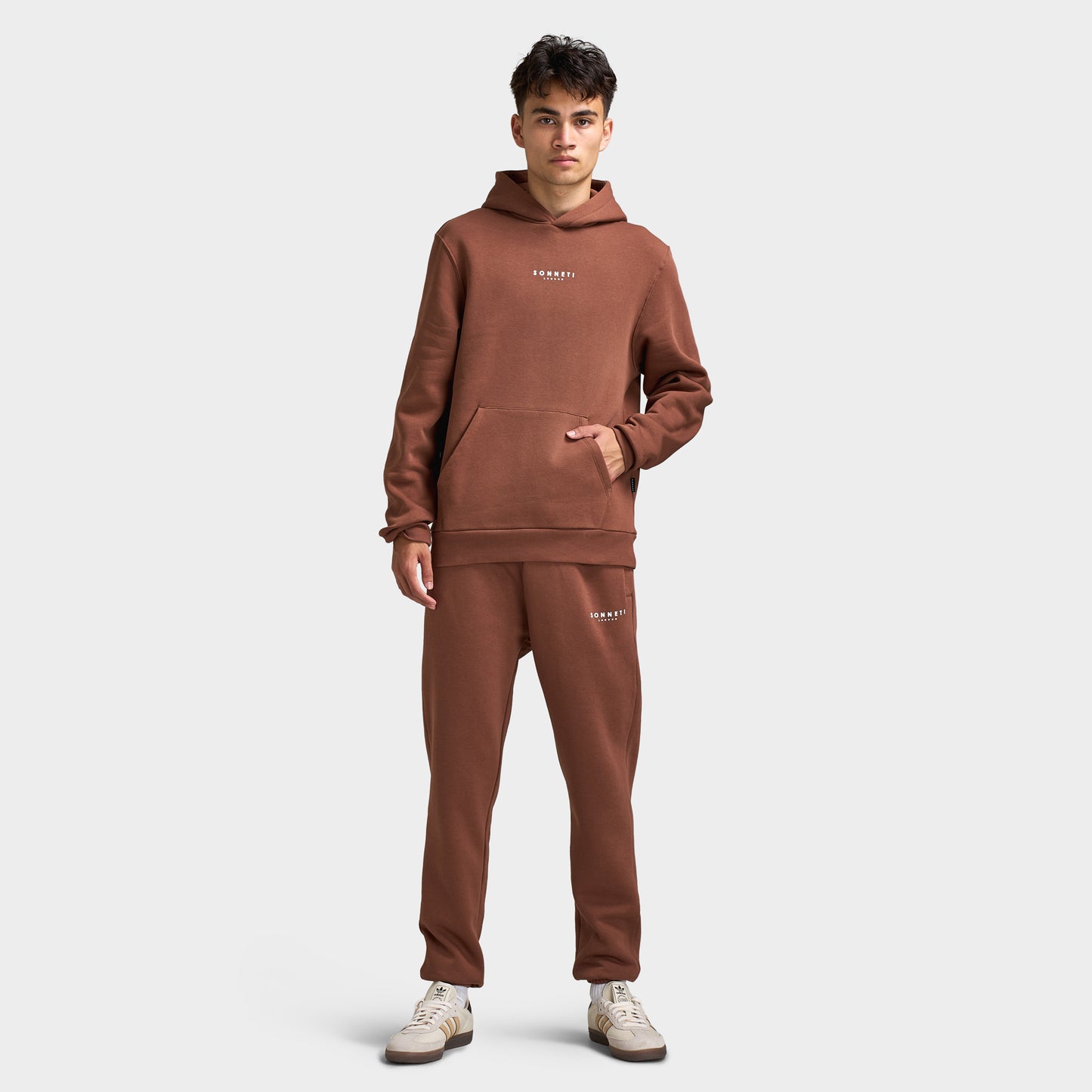 Sonneti London Hoodie 2.0. Full-body front view of model wearing cocoa brown hoodie with matching pants and white sneakers.
