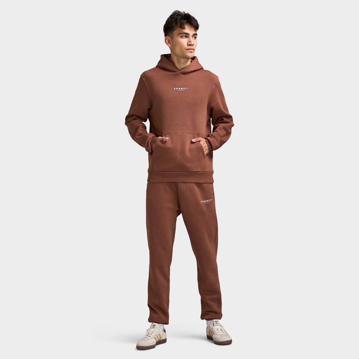 Sonneti London Hoodie 2.0. Full-body view of model wearing cocoa brown hoodie with matching pants and white sneakers.