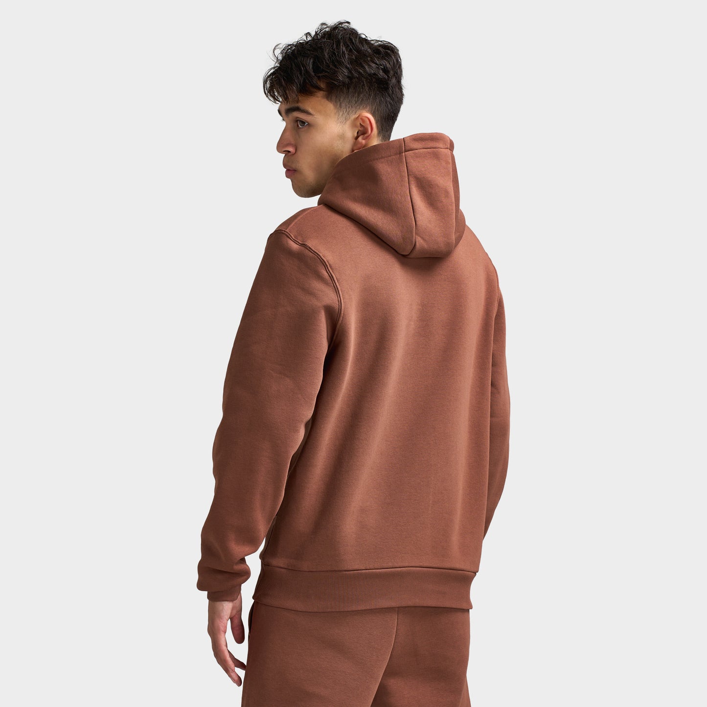 Sonneti London Hoodie 2.0. Back three-quarter view of model wearing cocoa brown hoodie with raised hood and relaxed fit.
