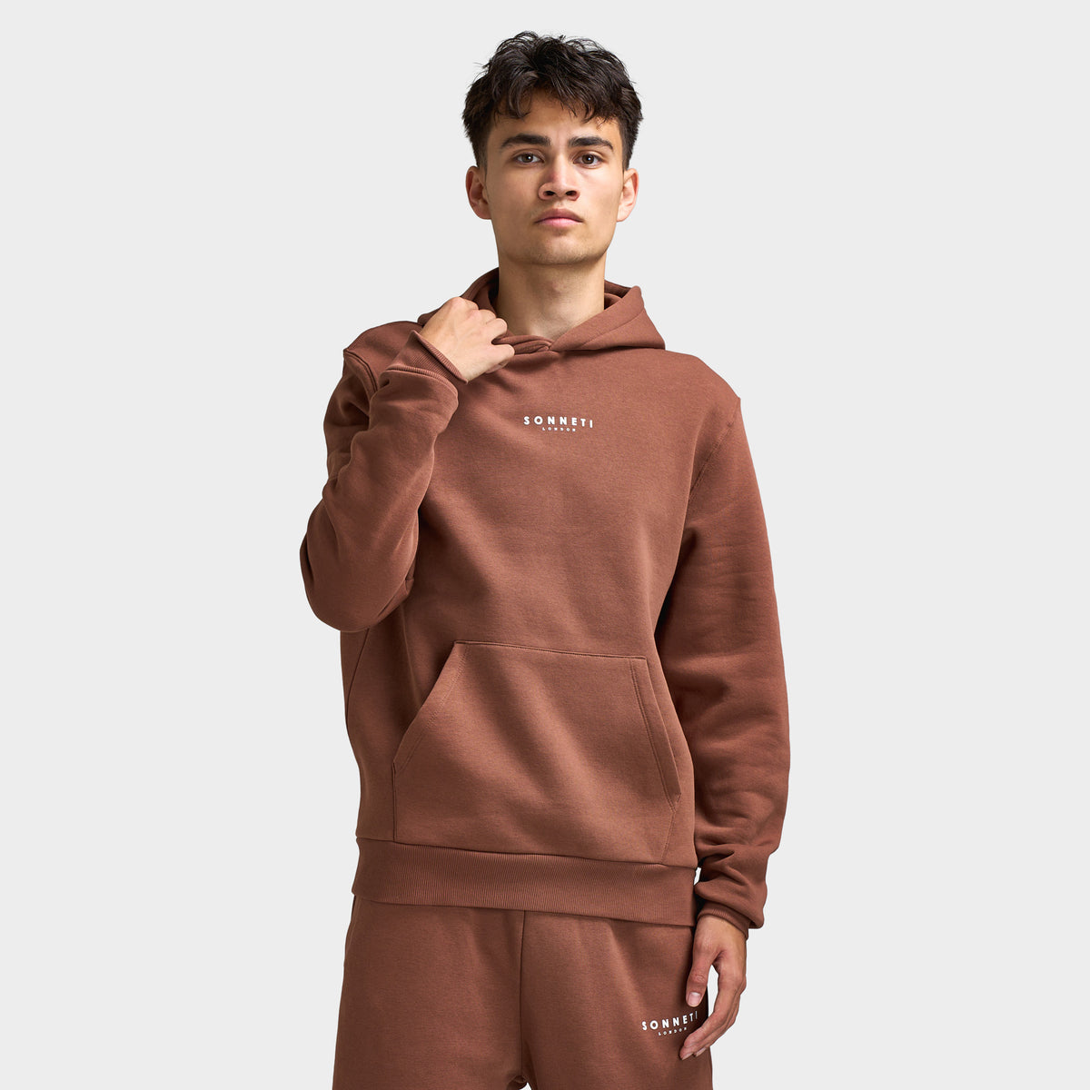Sonneti London Hoodie 2.0. Front view of model wearing cocoa brown hoodie with kangaroo pocket, drawstring hood and small white Sonneti chest branding.