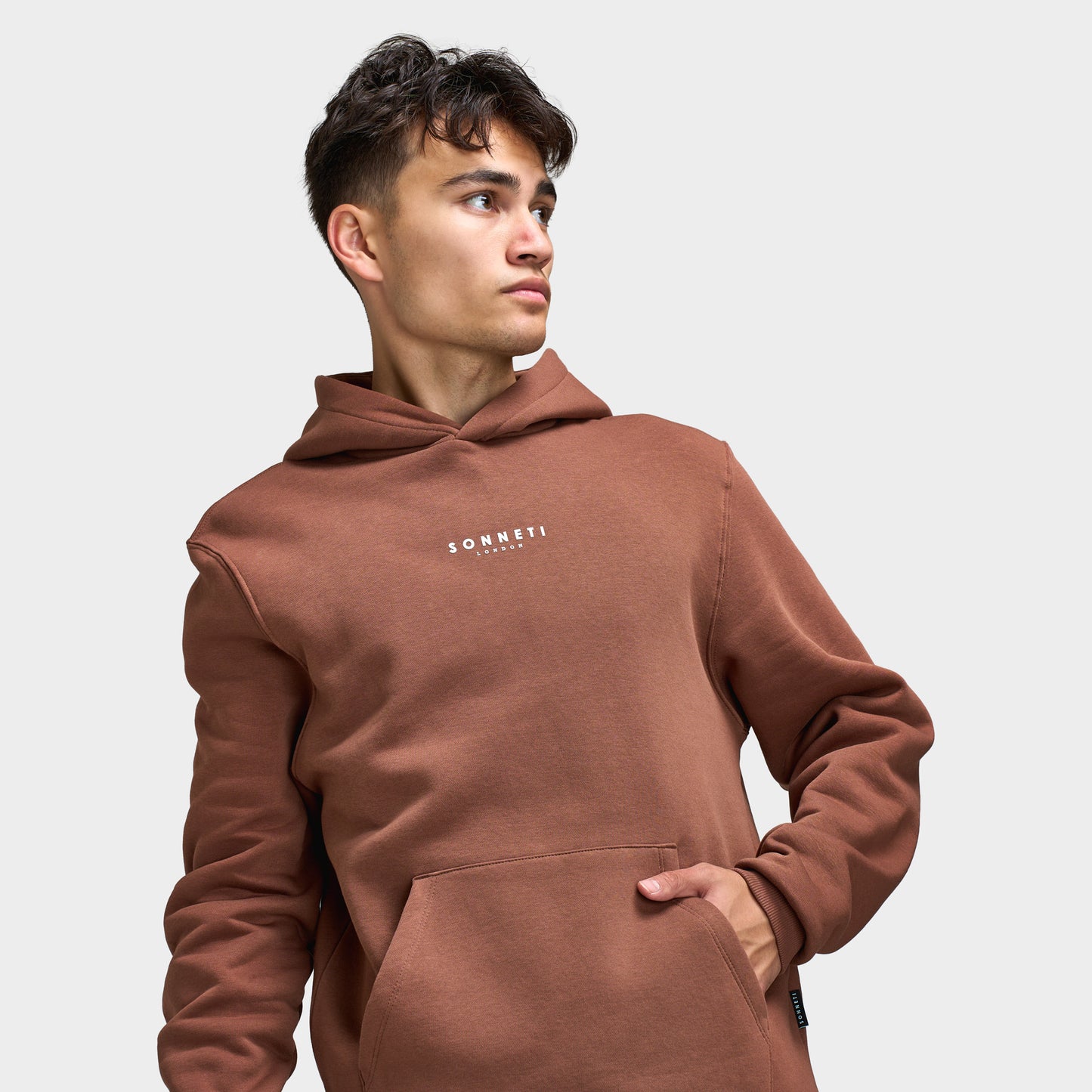 Sonneti London Hoodie 2.0. Three-quarter view of model wearing cocoa brown hoodie with kangaroo pocket and relaxed sleeves.