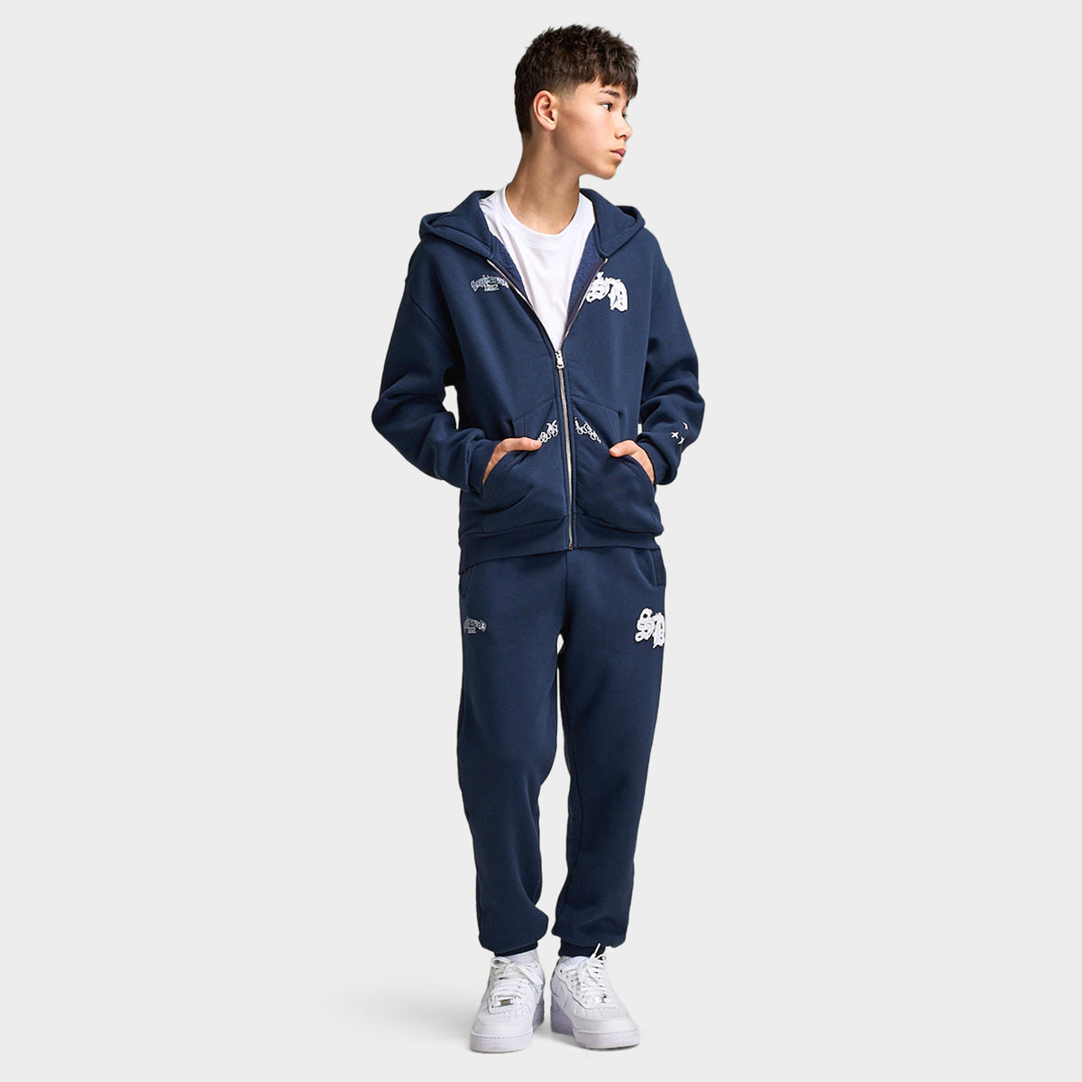 Supply & Demand Juniors' Scape Hoodie. Full-body front view of model wearing washed navy hoodie with matching pants and white sneakers.