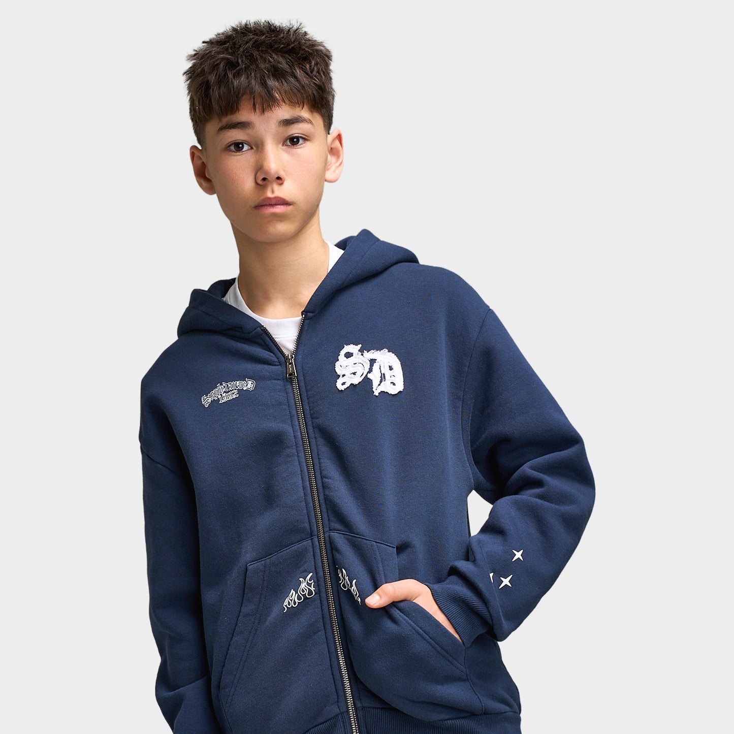 Supply & Demand Juniors' Scape Hoodie. Three-quarter view of model wearing washed navy full-zip hoodie with front pockets and white chest graphic.