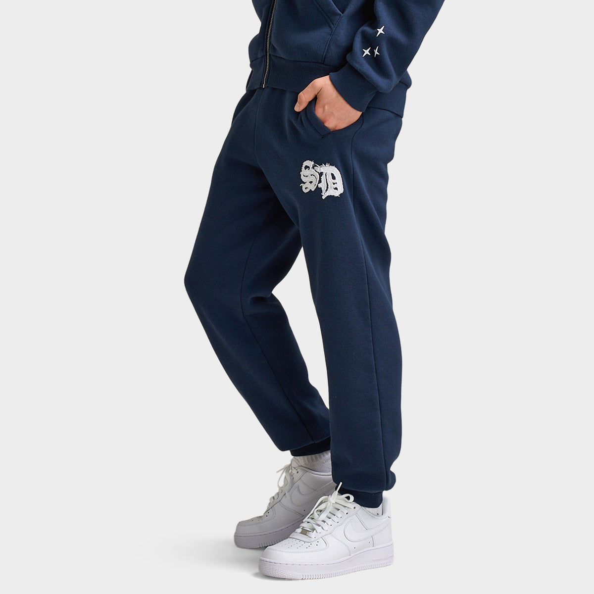 Supply & Demand Juniors' Scape Pants. Side view of model wearing washed navy pants with tapered legs, side pocket and white thigh graphic.