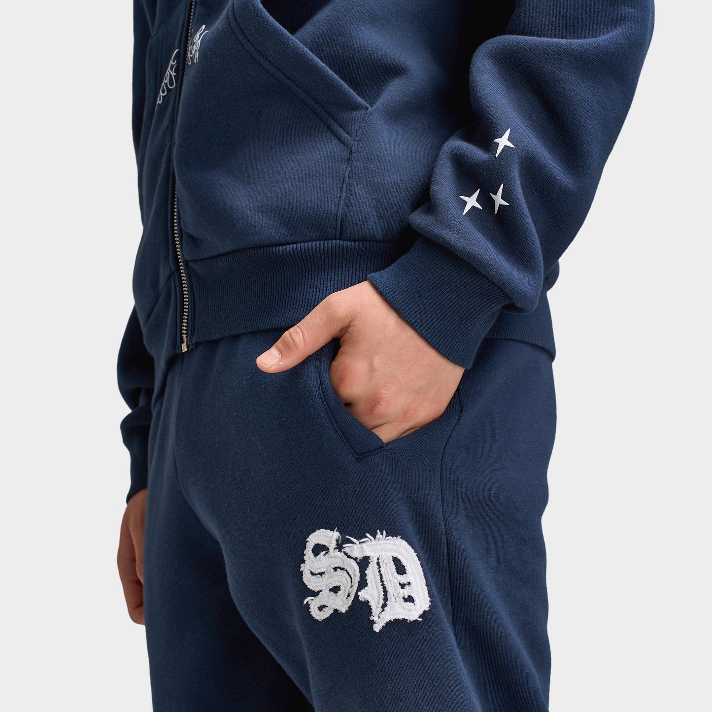 Supply & Demand Juniors' Scape Pants. Close-up of washed navy pants showing side pocket, elastic waistband and white graphic branding.