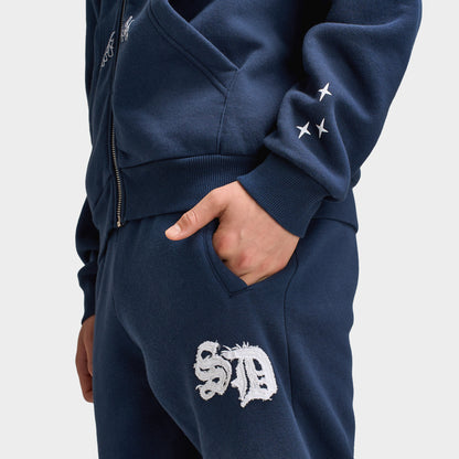 Supply & Demand Juniors' Scape Pants. Close-up of washed navy pants showing side pocket, elastic waistband and white graphic branding.