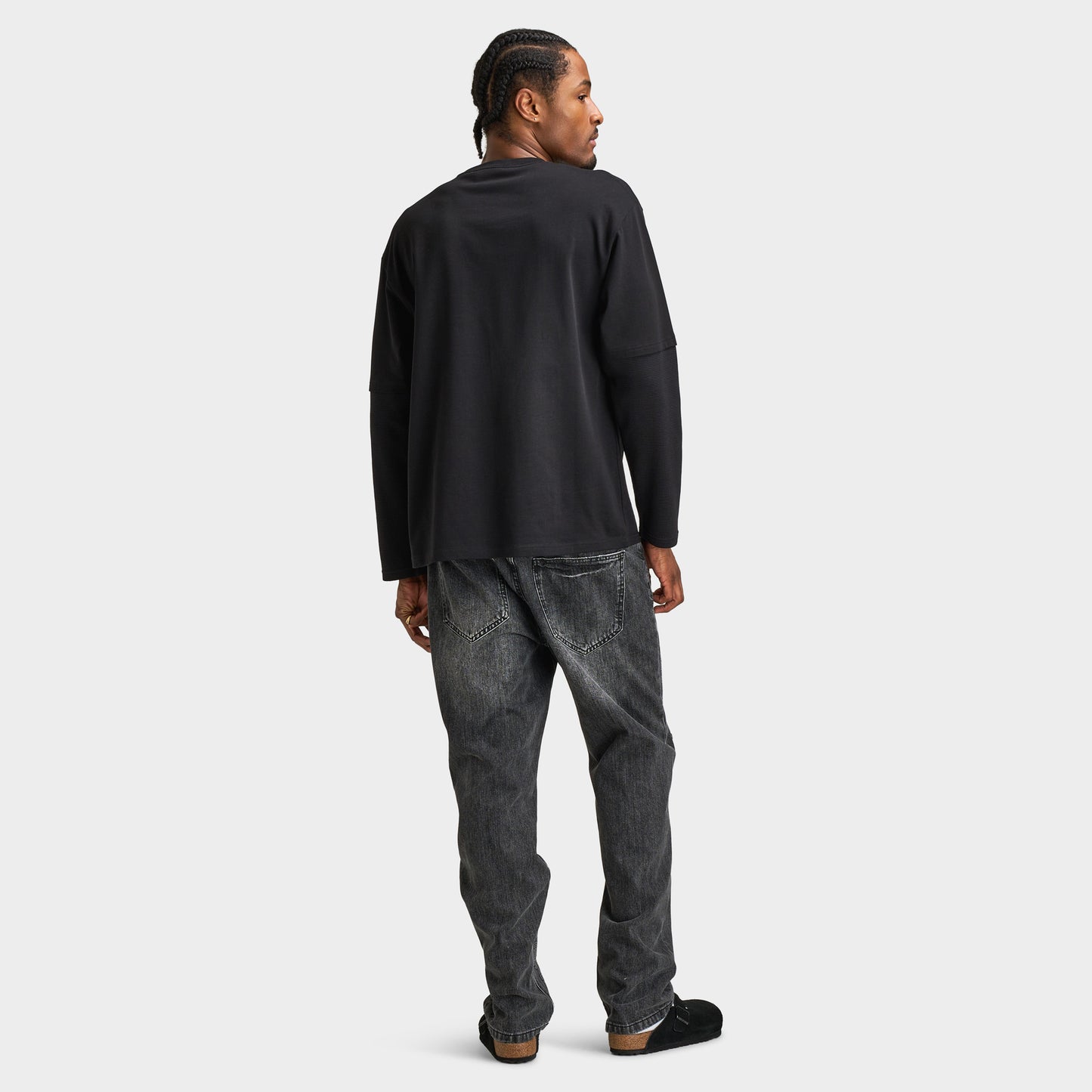 Supply & Demand Global Longsleeve Tee. Full-body back view of model wearing black long-sleeve T-shirt with distressed black jeans and dark shoes.