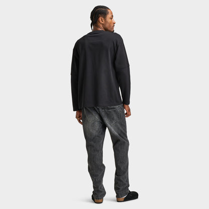 Supply & Demand Global Longsleeve Tee. Full-body back view of model wearing black long-sleeve T-shirt with distressed black jeans and dark shoes.