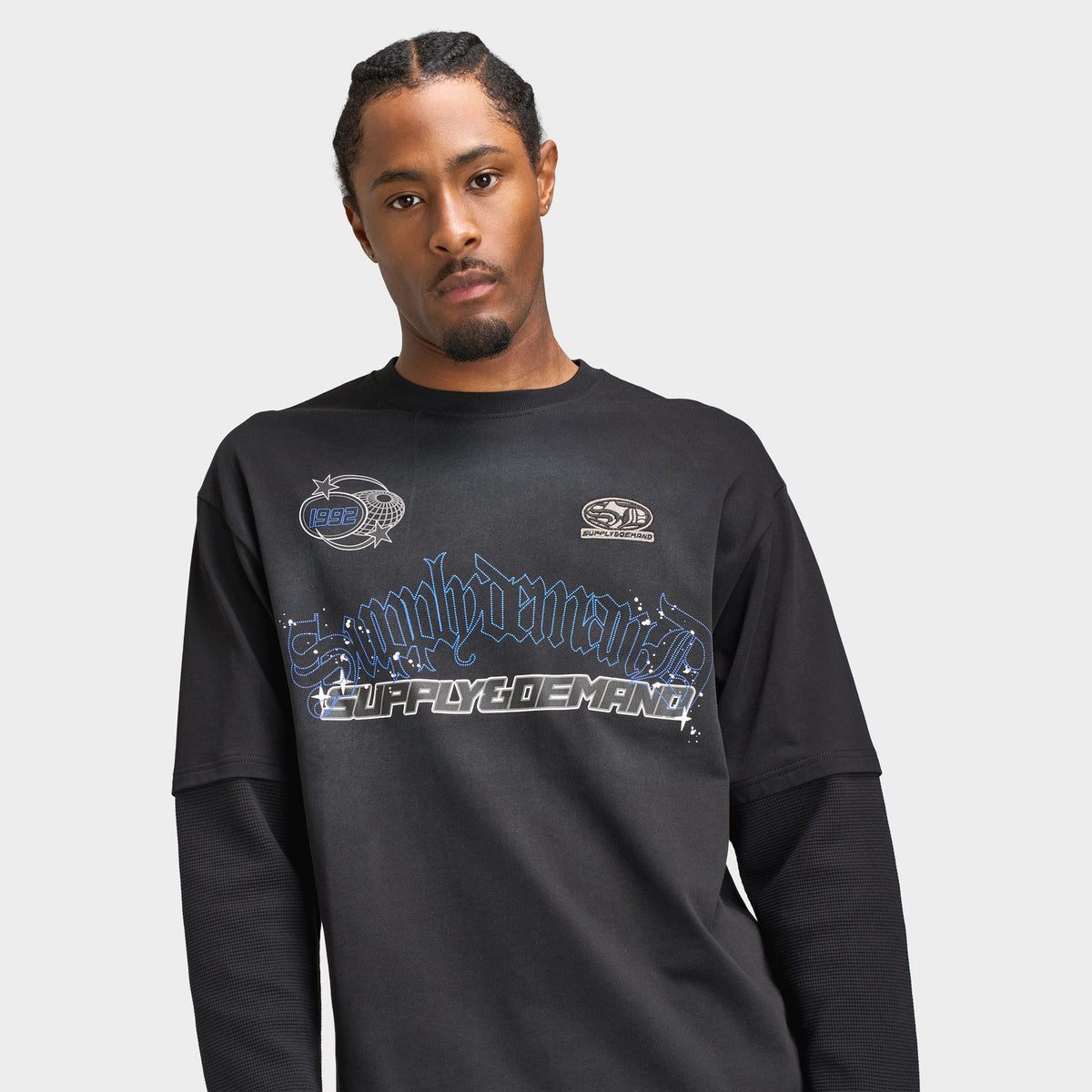 Supply & Demand Global Longsleeve Tee. Three-quarter view of model wearing black long-sleeve T-shirt with printed chest graphic and relaxed sleeves.