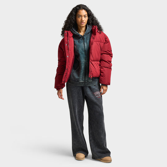 Supply & Demand Women's Macy Jacket. Full-body front view of model wearing pomegranate puffer jacket with dark pants and sneakers.