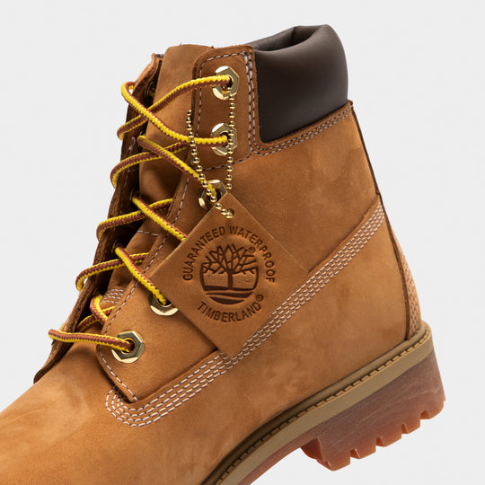 Timberland Juniors' 6" Premium Lace Up Waterproof Boot. Close-up of wheat junior boot showing yellow laces, metal eyelets, padded black collar and Timberland tree logo.