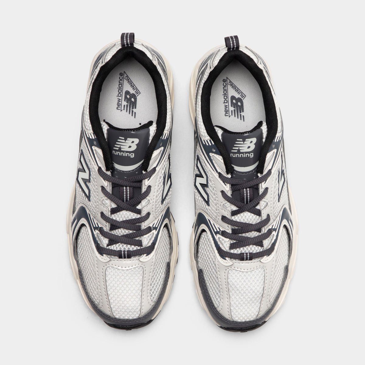 New Balance 530. Top view of sea salt and magnet sneakers showing grey laces, padded tongues and mesh toe boxes.