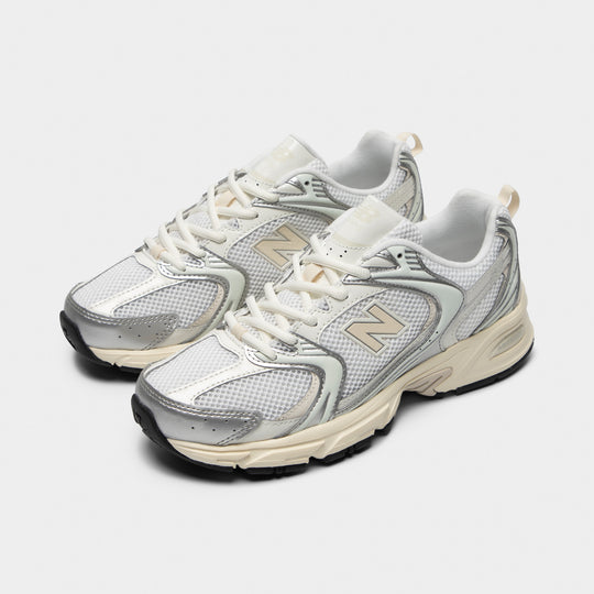 New Balance 530. Three-quarter view of silver metallic and linen sneakers with cream laces, layered overlays and neutral-toned detailing.