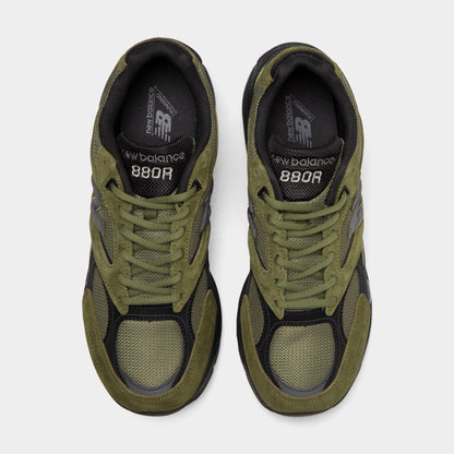 New Balance 880. Top-down overhead view of a pair of low-top sneakers displaying dark mesh toe boxes with wakame olive green suede mudguards, wakame green laces, black tongues with silver logos, and dark grey insoles with "NB" prints. 