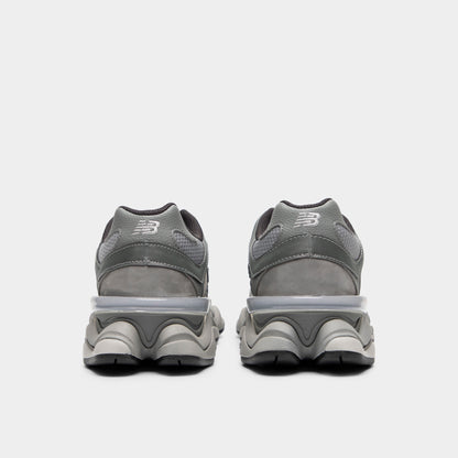 New Balance 9060. Rear view of a pair of chunky sneakers displaying slate grey suede heel counters with silver "NB" embroidery, translucent CR heel clips, dark grey padded collar linings, and exaggerated sculpted pod midsoles. 