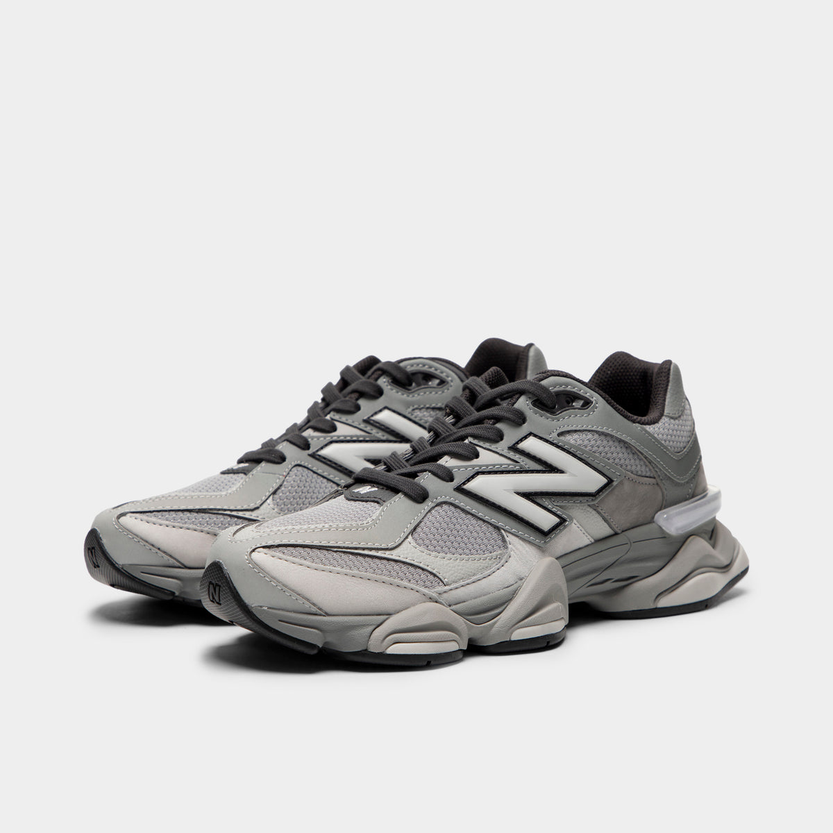 New Balance 9060. Three-quarter view of a pair of chunky lifestyle sneakers showing harbor grey mesh uppers, slate grey suede overlays, silver midfoot "N" logos, dark grey laces, translucent heel clips, and thick sculpted dual-density midsoles. 