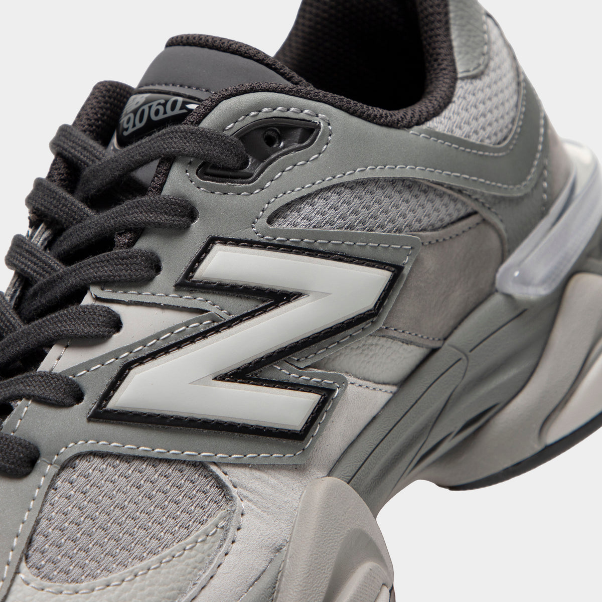 New Balance 9060. Close-up view of midfoot and collar highlighting harbor grey mesh base, slate grey suede overlays, silver and black "N" logo, dark grey laces, and clear plastic heel counter clip. 