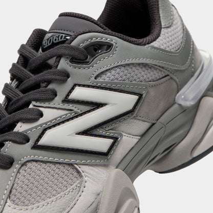 New Balance 9060. Close-up view of midfoot and collar highlighting harbor grey mesh base, slate grey suede overlays, silver and black "N" logo, dark grey laces, and clear plastic heel counter clip. 
