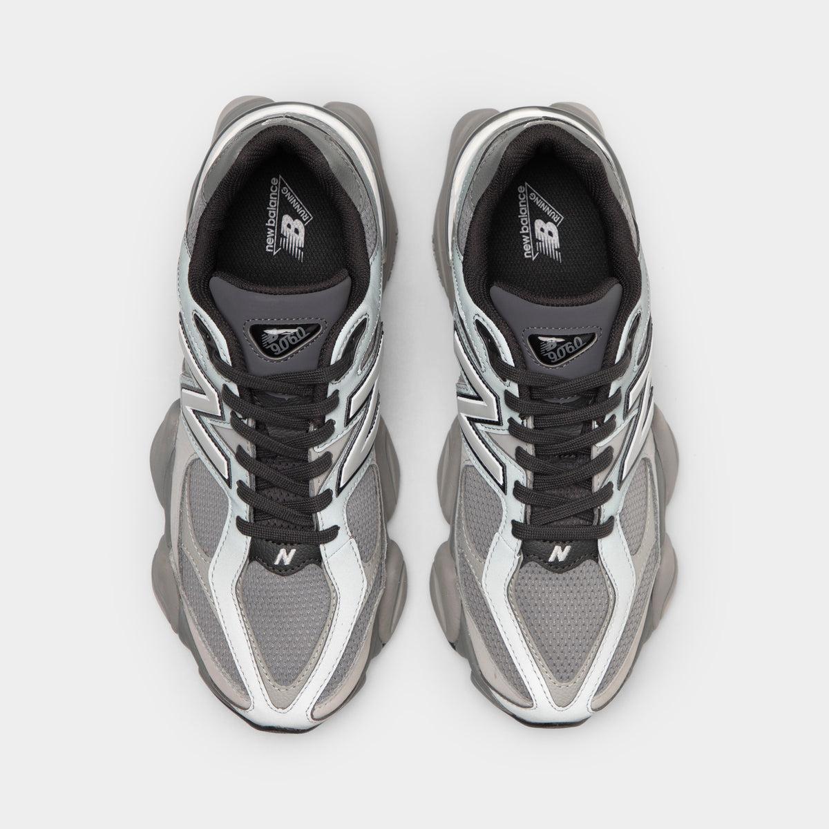 New Balance 9060. Top-down overhead view of a pair of sneakers displaying harbor grey mesh toe boxes with slate grey suede toe overlays, dark grey laces, dark grey tongues with triangular "NB 9060" jewel patches, and black insoles with white logo prints. 