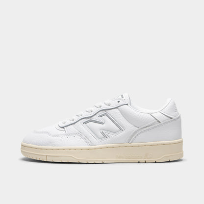 New Balance 950. Side view of low-top sneakers featuring a white leather upper, white padded leather "N" logo on the midfoot with tonal stitching, white laces, white padded collar, off-white aged rubber cupsole, and an off-white rubber outsole. 