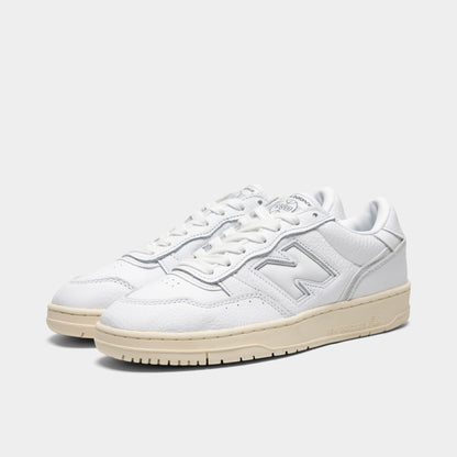New Balance 950. Three-quarter view of a pair of low-top sneakers showing white leather uppers, midfoot "N" logos, white laces, padded collars, and off-white aged rubber soles. 