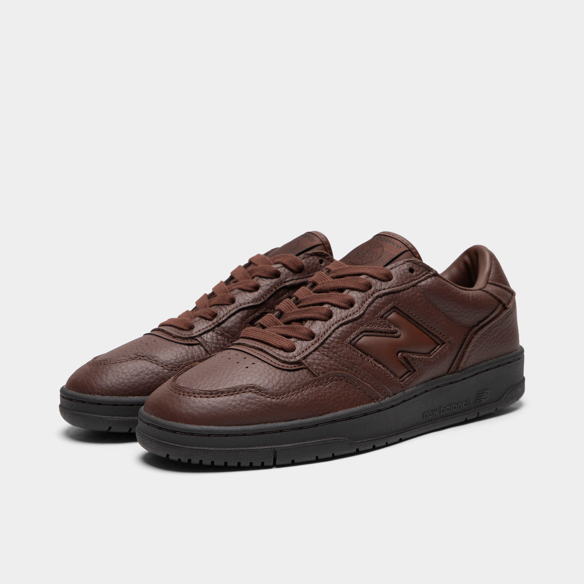 New Balance 950. Three-quarter view of a pair of low-top sneakers showing dark brown tumble leather uppers, midfoot "N" logos, dark brown laces, padded collars, and black rubber soles. 