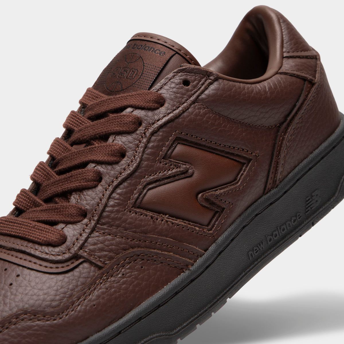 New Balance 950. Close-up view of toe box, midfoot, and collar highlighting dark brown tumble leather construction, brown "N" midfoot logo, brown laces, tonal stitching, and black rubber midsole edge. 