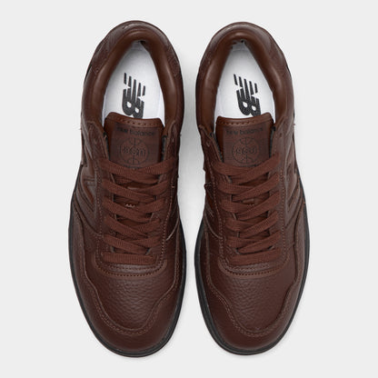 New Balance 950. Top-down overhead view of a pair of low-top sneakers displaying dark brown tumble leather toe boxes, dark brown laces, leather tongues with debossed logo patches, and white insoles with dark "NB" branding. 