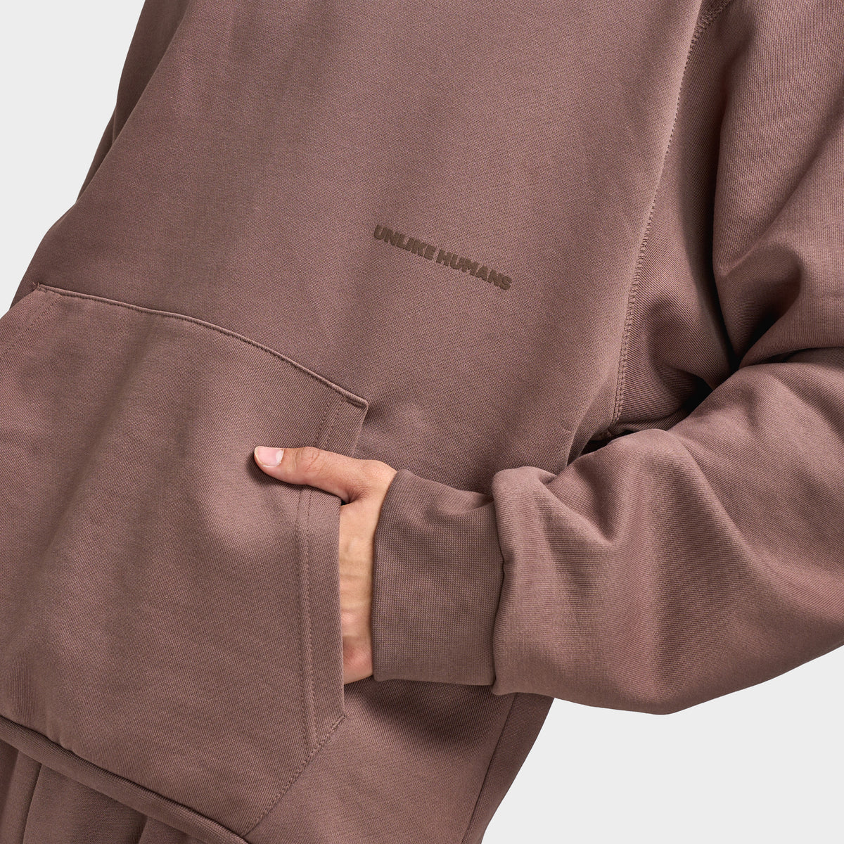 Unlike Humans Ridge Hoodie. Close-up of coffee quarts hoodie showing kangaroo pocket, ribbed cuff and soft brushed fabric texture.