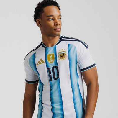 Man wears adidas Men's Argentina Home Messi Jersey “White / Icy Blue – Light Blue” jersey. Shop World Cup now at JD Sports.