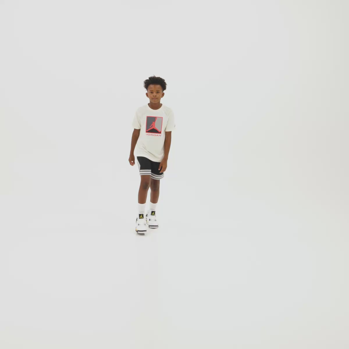 Jordan 4 Retro GS. Video thumbnail showing model standing against a light grey studio background wearing white t-shirt, shorts, showcasing the removable velcro tongue tag.